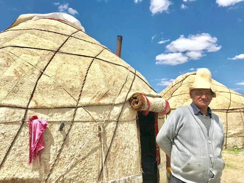 A Kyrgyz man stands outside of his yurt, wearing a kalpak. Photo credit: Michel Behar